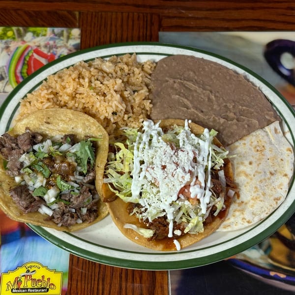 Two tacos, rice, and refried beans on a white plate with a green rim from Taqueria Mi Pueblo.