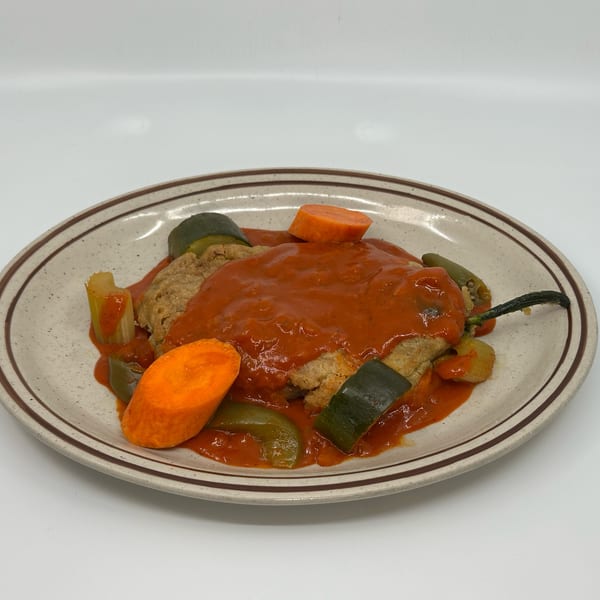 A Mexican chile relleno dish with red sauce, carrots, and zucchini on an oval plate.