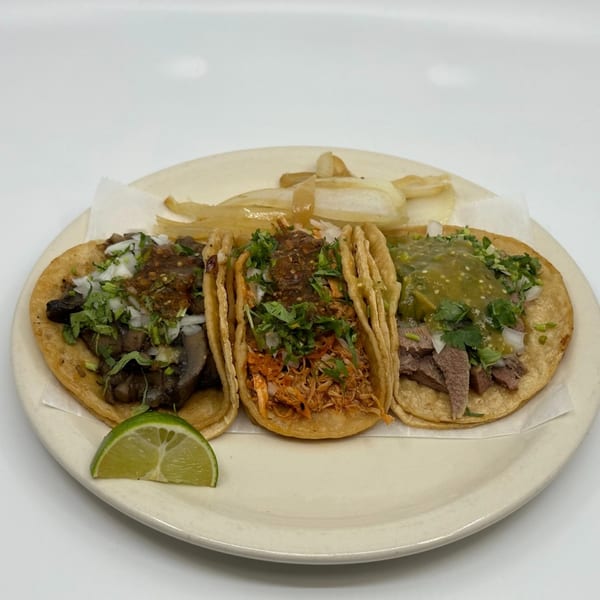 Three Taqueria Mi Pueblo tacos with various fillings, onions, cilantro, salsa, and a lime wedge.