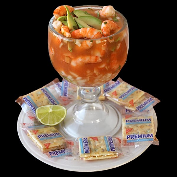 Shrimp cocktail in a goblet with avocado, lime, and Premium crackers on a white plate.