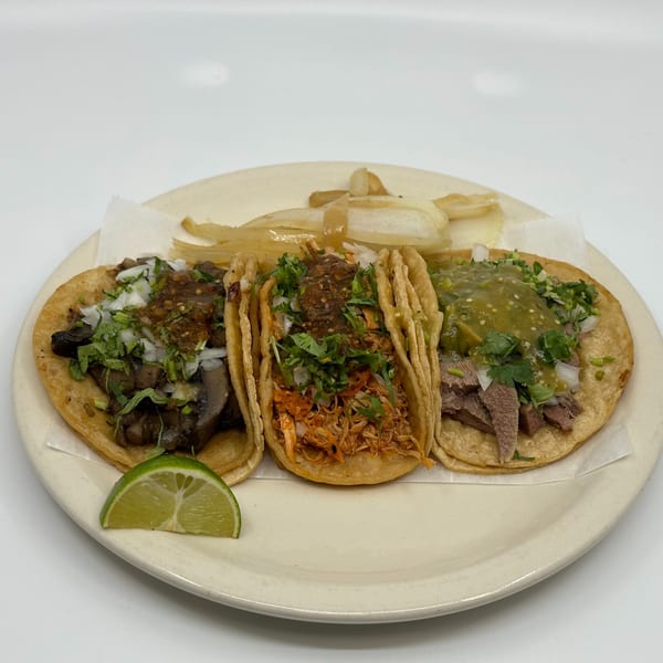 Three Taqueria Mi Pueblo tacos with various fillings, onions, cilantro, and salsa, with a lime wedge.